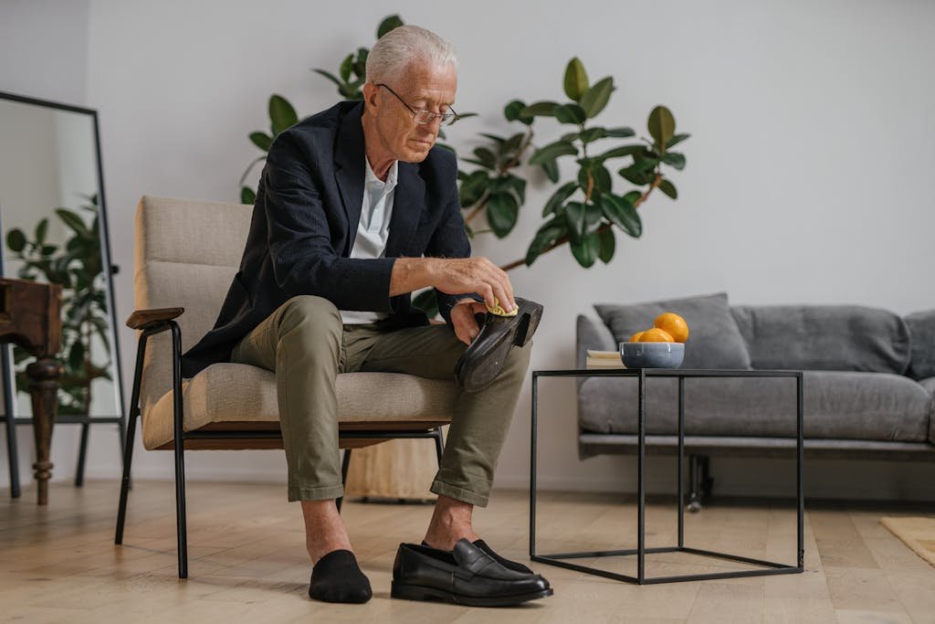 Elderly man polishing shoes at home. Lifestyle and daily grooming indoors.